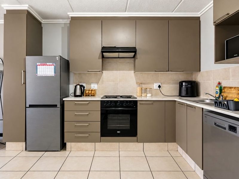 A functional kitchen featuring modern taupe cabinetry, tiled backsplash, built-in oven with hob, and tiled flooring.
