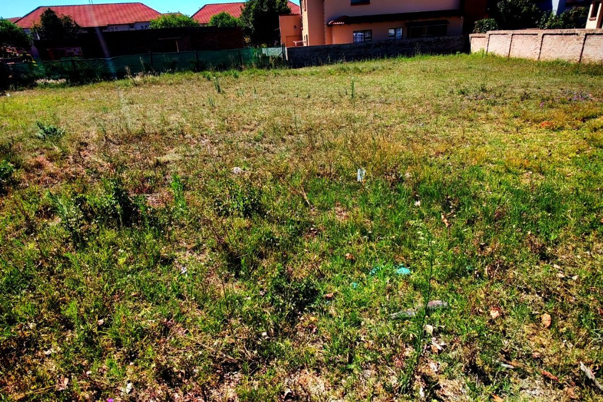A vacant residential plot featuring natural grass coverage, enclosed by boundary walls and fencing, situated in a developed neighborhood.
