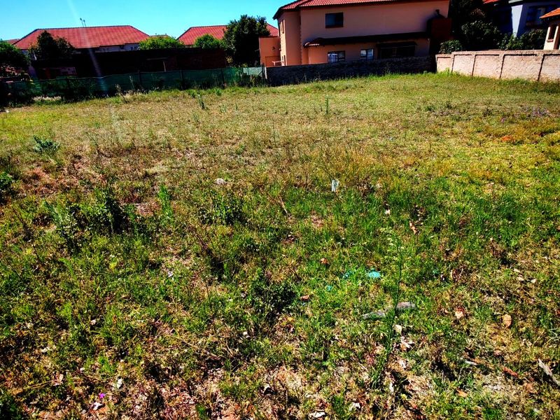 A vacant residential plot featuring natural grass coverage, enclosed by boundary walls and fencing, situated in a developed neighborhood.