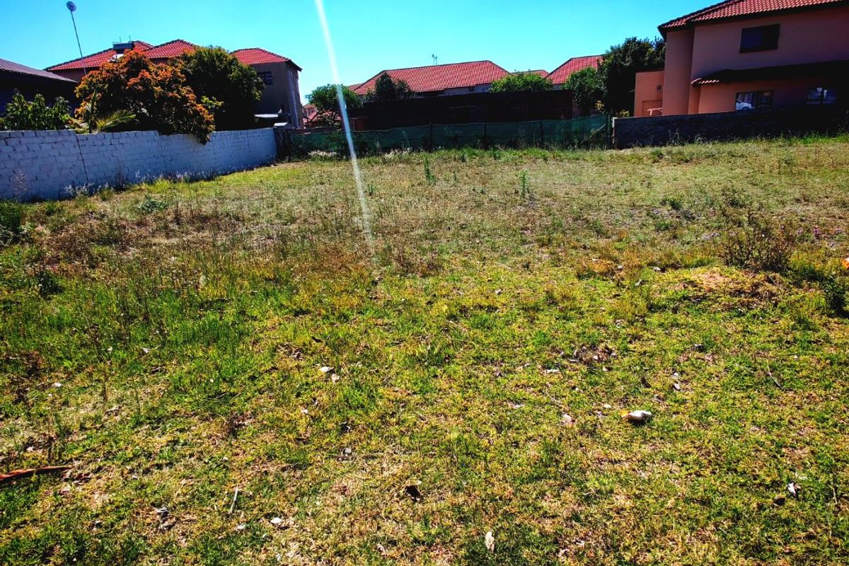 A vacant residential plot of land featuring perimeter walling and fencing, situated in a developed suburban neighborhood.
