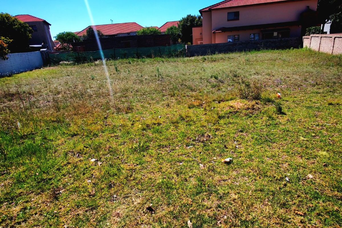 A vacant residential plot of land featuring grass coverage and perimeter boundary walls, situated in a developed suburban neighborhood.