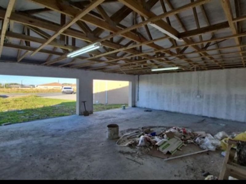 Spacious unfinished garage area featuring exposed timber roof trusses, concrete flooring, and open access to the exterior.