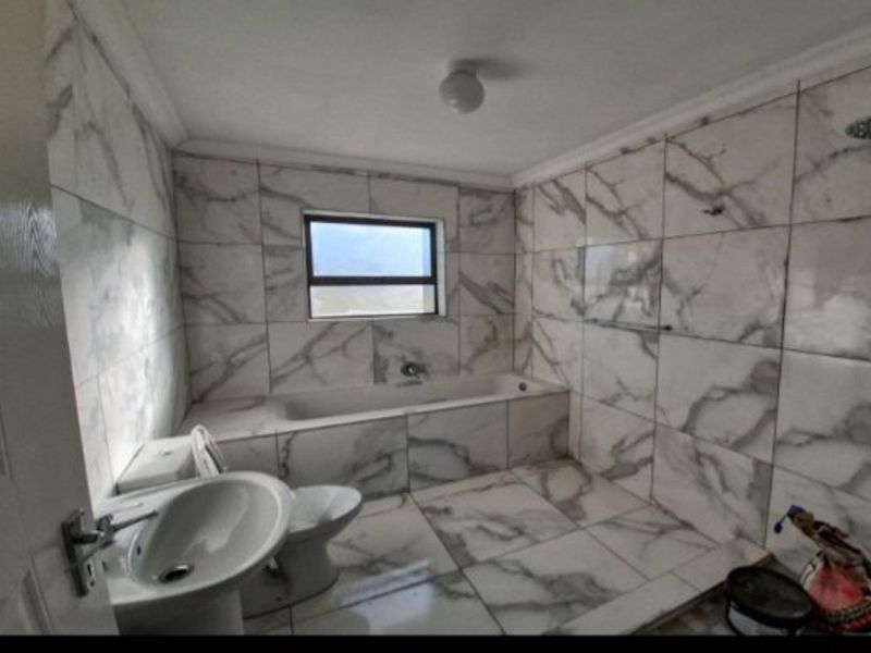 A modern bathroom featuring floor-to-ceiling marble-look tiling, a built-in bathtub, a pedestal basin, and a shower fixture.