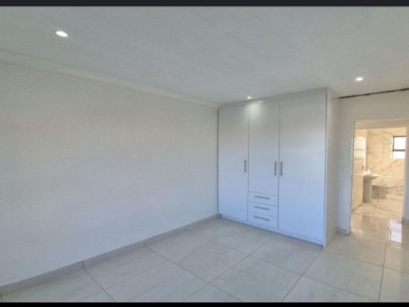 A bright, empty bedroom featuring modern tiled flooring, built-in cupboards, and direct access to an en-suite bathroom.