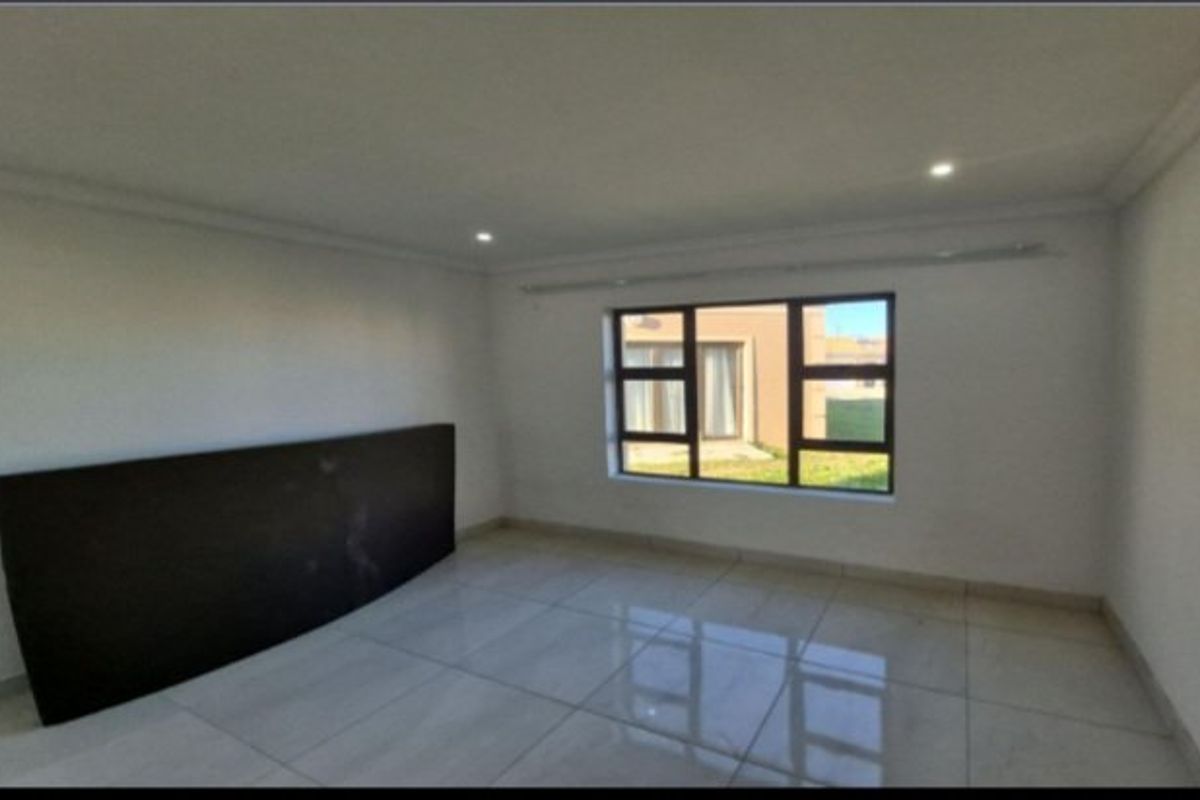 A bright, empty living room featuring large aluminium-framed windows, polished tiled flooring, and modern recessed downlighting.