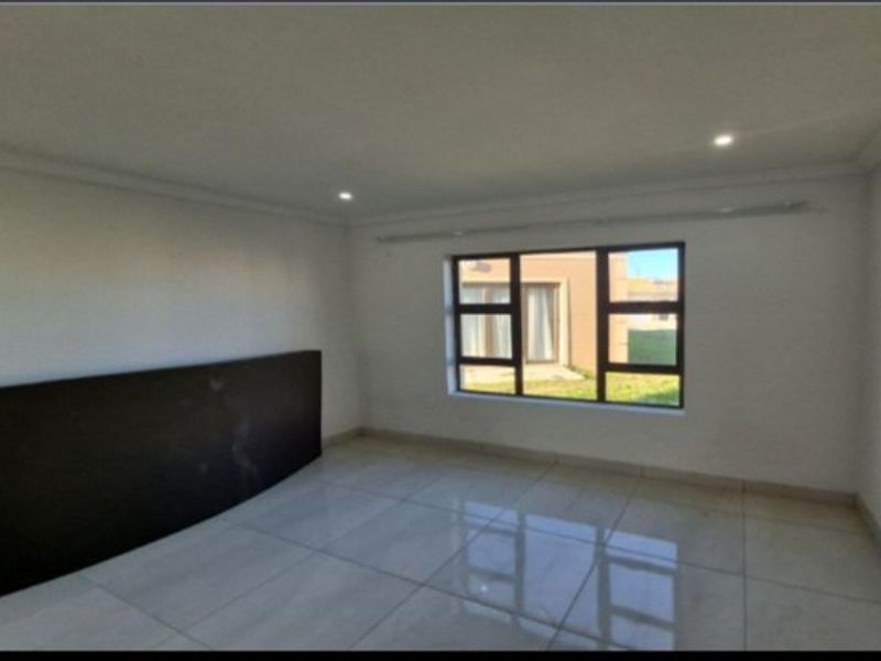 A bright, empty living room featuring large aluminium-framed windows, polished tiled flooring, and modern recessed downlighting.