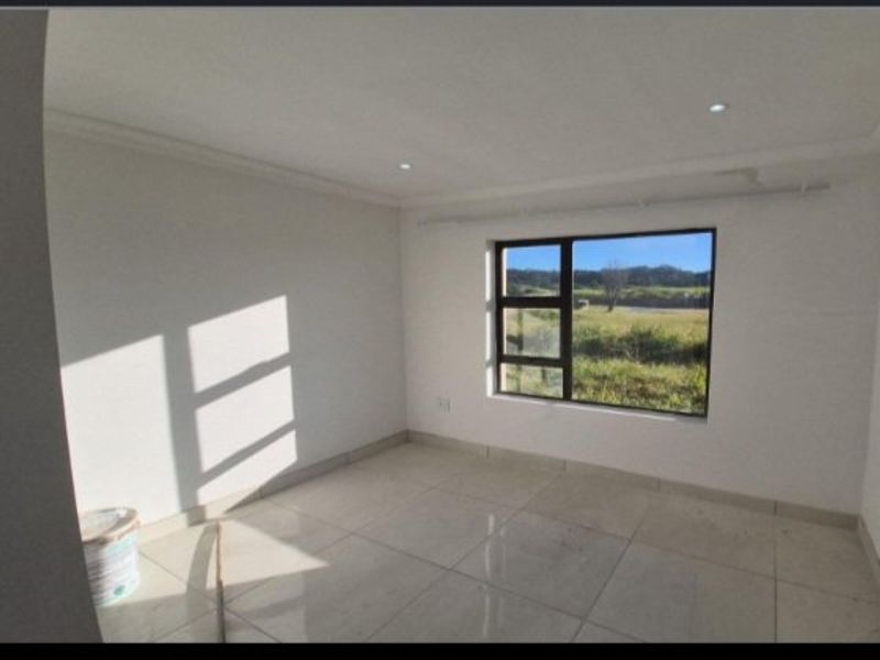 A bright, empty bedroom featuring neutral tiled flooring, recessed downlights, and a large aluminium-framed window with views of the surrounding landscape.