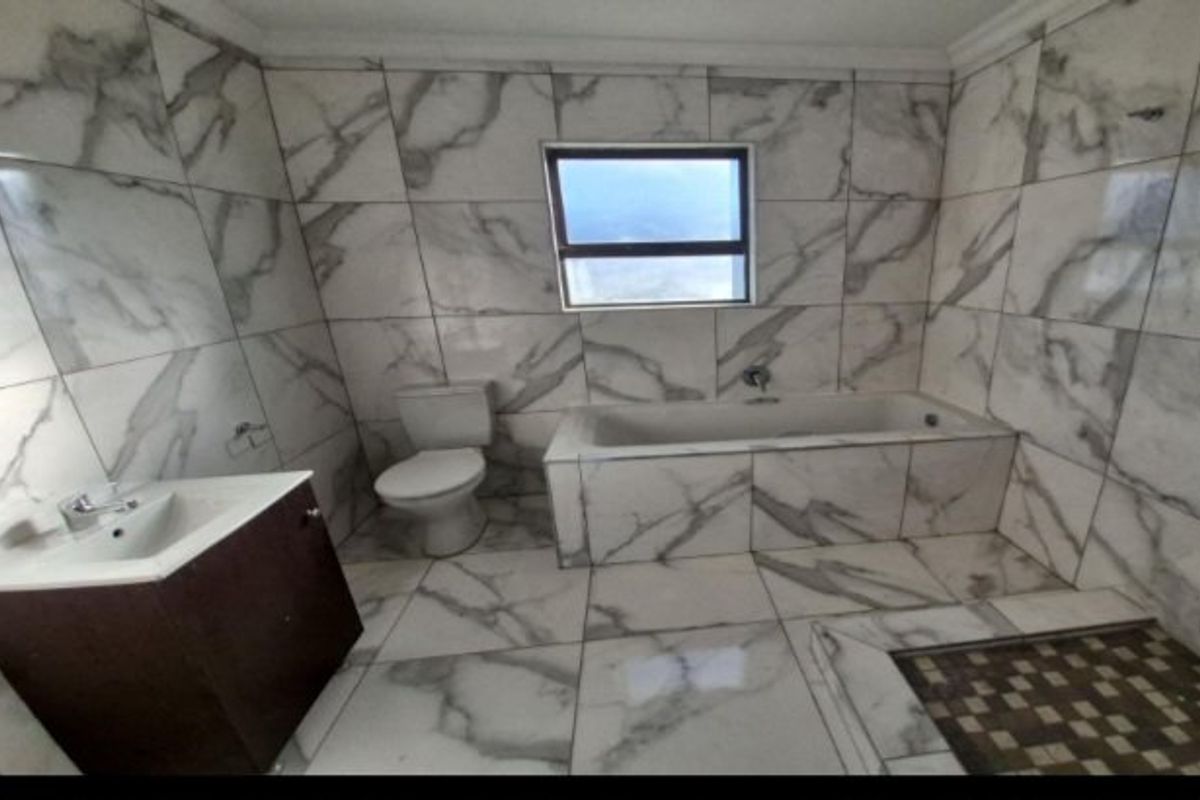 A modern bathroom featuring marble-look wall and floor tiles, a built-in bathtub, a vanity cabinet with a basin, and a separate shower area.