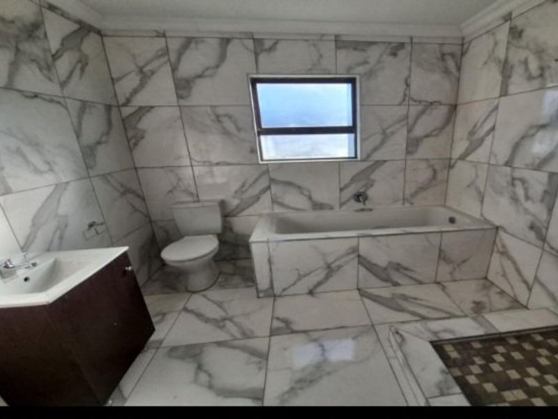 A modern bathroom featuring marble-look wall and floor tiles, a built-in bathtub, a vanity cabinet with a basin, and a separate shower area.