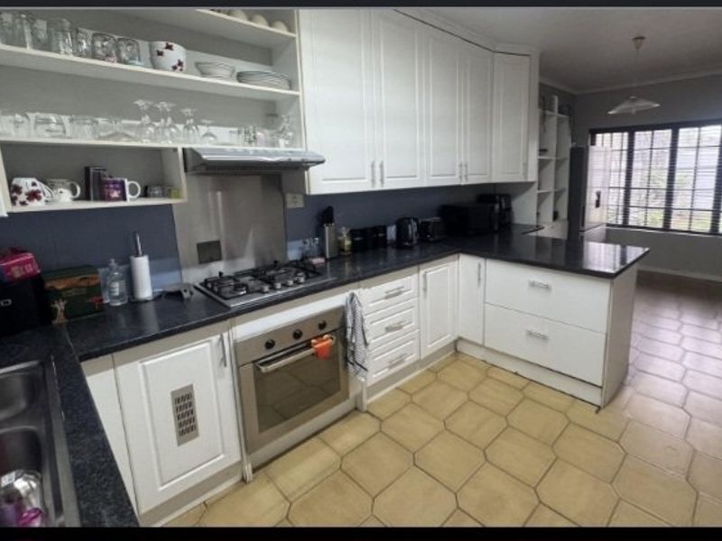 A functional kitchen featuring white cabinetry, dark laminate countertops, a gas hob with extractor, and tiled flooring, offering a practical layout for daily use.