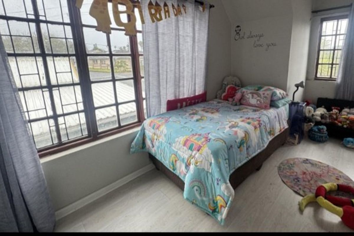 A bedroom featuring laminate flooring and windows fitted with security bars, providing natural light and a functional living space.