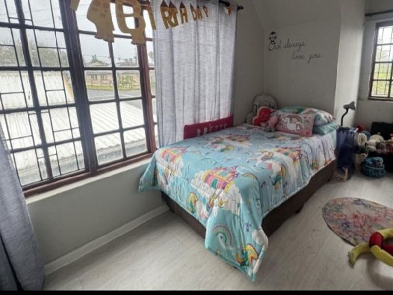 A bedroom featuring laminate flooring and windows fitted with security bars, providing natural light and a functional living space.