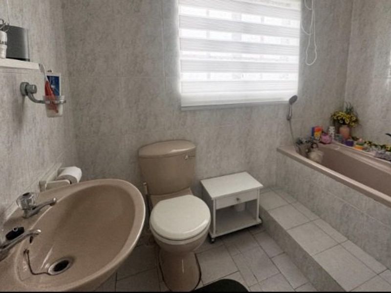 A functional bathroom featuring a built-in bathtub, pedestal basin, and toilet with neutral wall and floor tiling.
