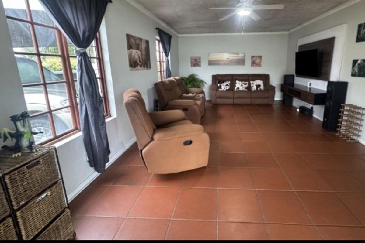 Spacious living room featuring terracotta floor tiles, a ceiling fan, and a built-in media wall unit.