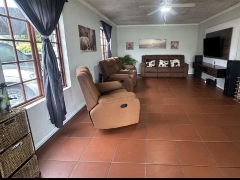Spacious living room featuring terracotta floor tiles, a ceiling fan, and a built-in media wall unit.