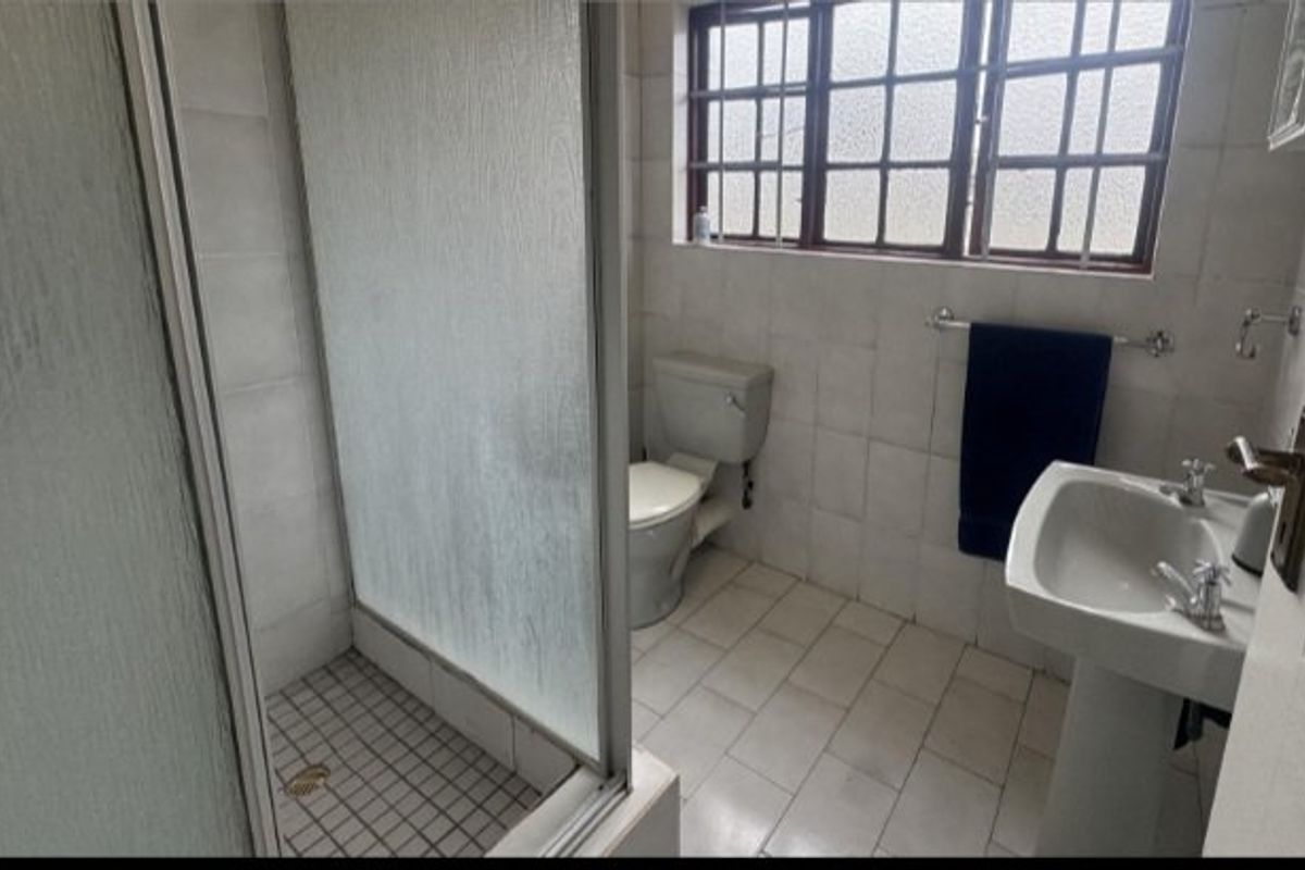 A functional bathroom featuring a shower enclosure, pedestal basin, and toilet, finished with tiled walls and flooring, ready for modernization.