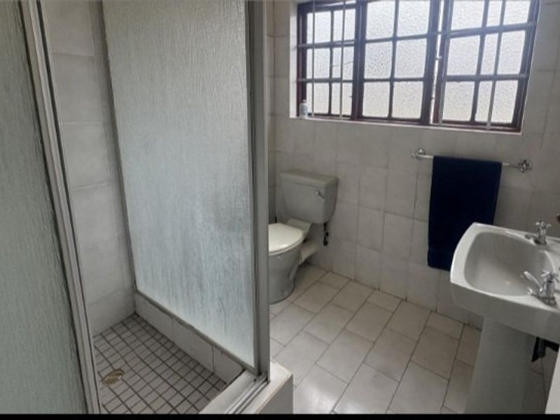 A functional bathroom featuring a shower enclosure, pedestal basin, and toilet, finished with tiled walls and flooring, ready for modernization.