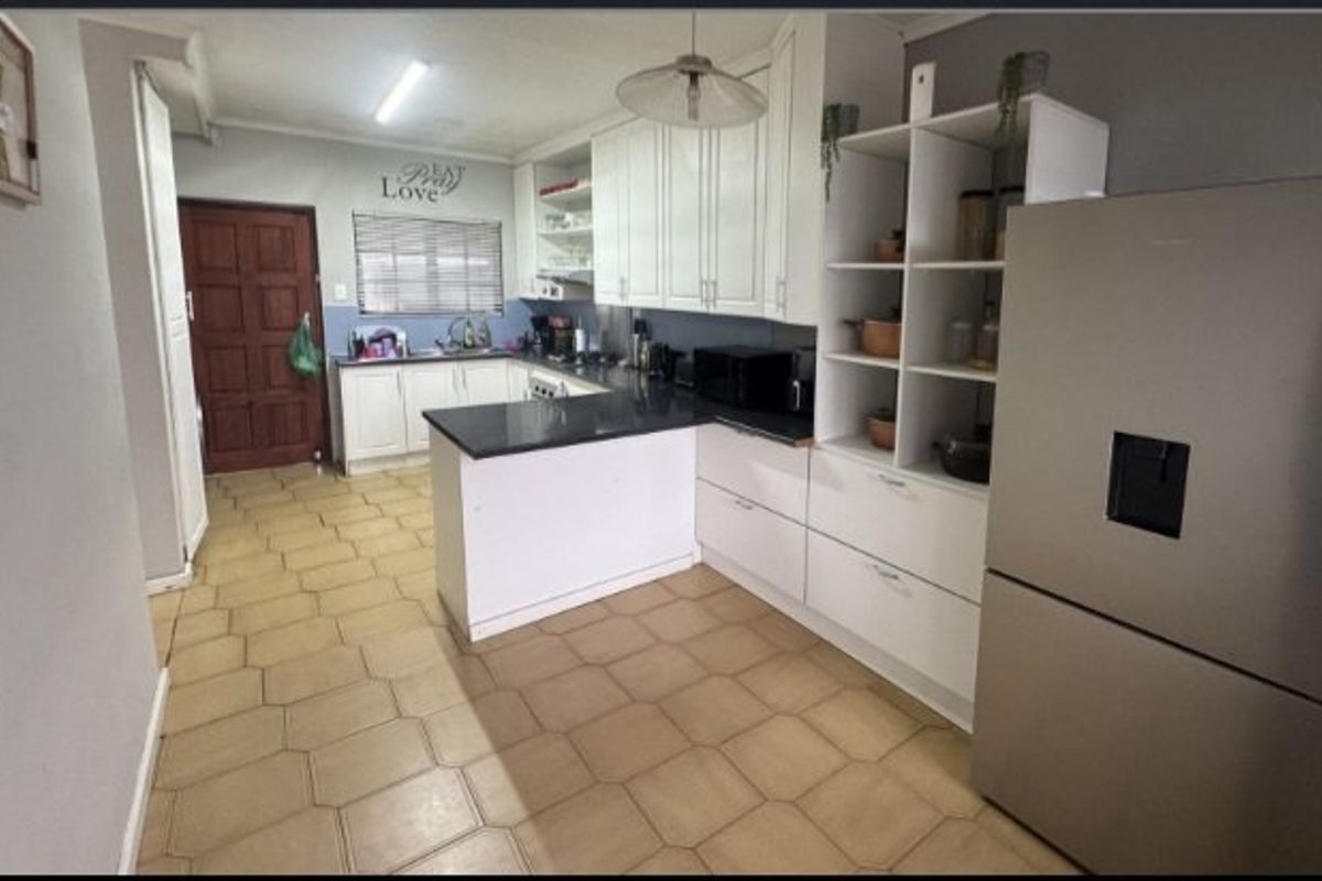 A functional kitchen featuring white built-in cabinetry, dark granite countertops, a double sink, and tiled flooring with an open-plan layout.