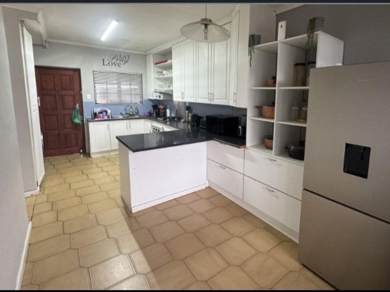 A functional kitchen featuring white built-in cabinetry, dark granite countertops, a double sink, and tiled flooring with an open-plan layout.