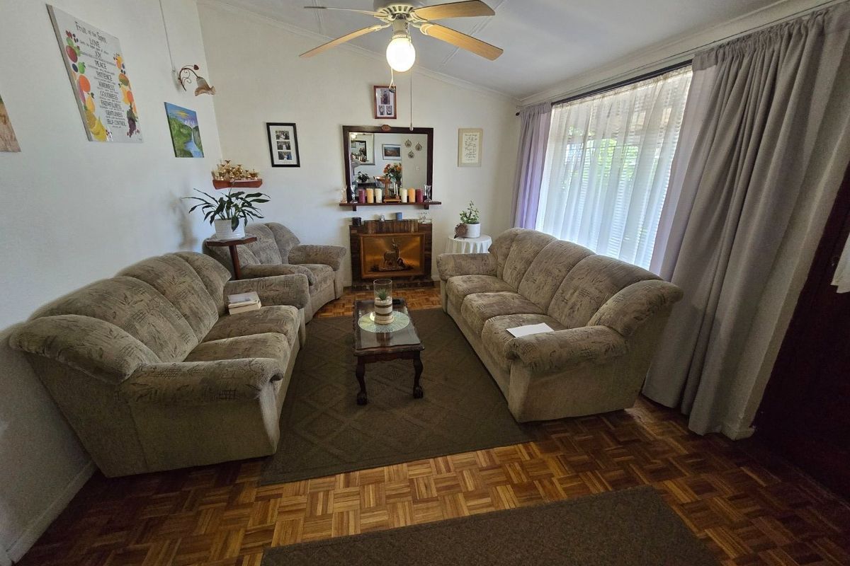 A cozy living room featuring classic parquet flooring, a central ceiling fan, and a fireplace, offering a warm and traditional atmosphere.