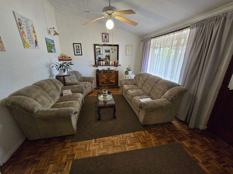 A cozy living room featuring classic parquet flooring, a central ceiling fan, and a fireplace, offering a warm and traditional atmosphere.