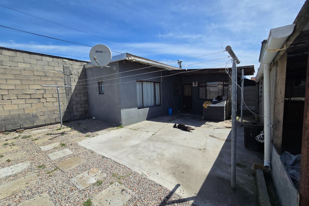 Rear exterior view of the property featuring a concrete patio area, cinder block boundary wall, and basic utility infrastructure.