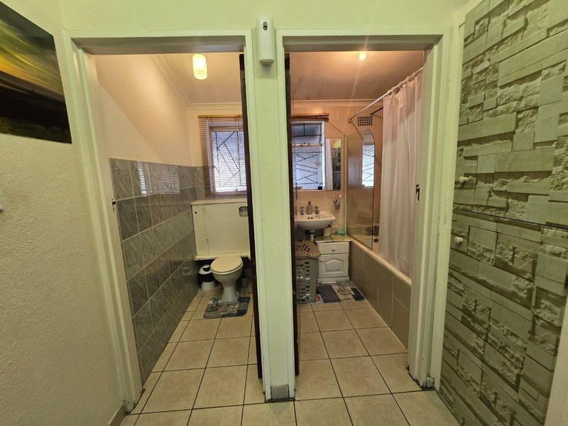 A split-layout bathroom featuring a separate toilet and a combined bath-shower area with tiled finishes and stone cladding accents.