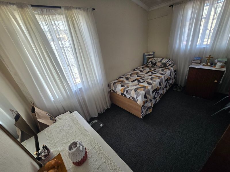 A functional bedroom featuring carpet flooring and dual windows equipped with security bars, providing natural light.