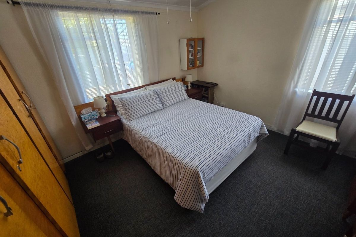 A functional bedroom featuring carpeted flooring, built-in wardrobe storage, and dual windows with curtain rails.