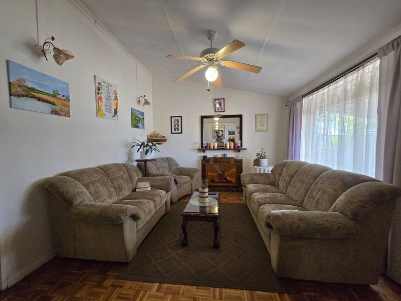 A comfortable living room featuring classic parquet flooring, a central ceiling fan, and a traditional fireplace with a mantelpiece.