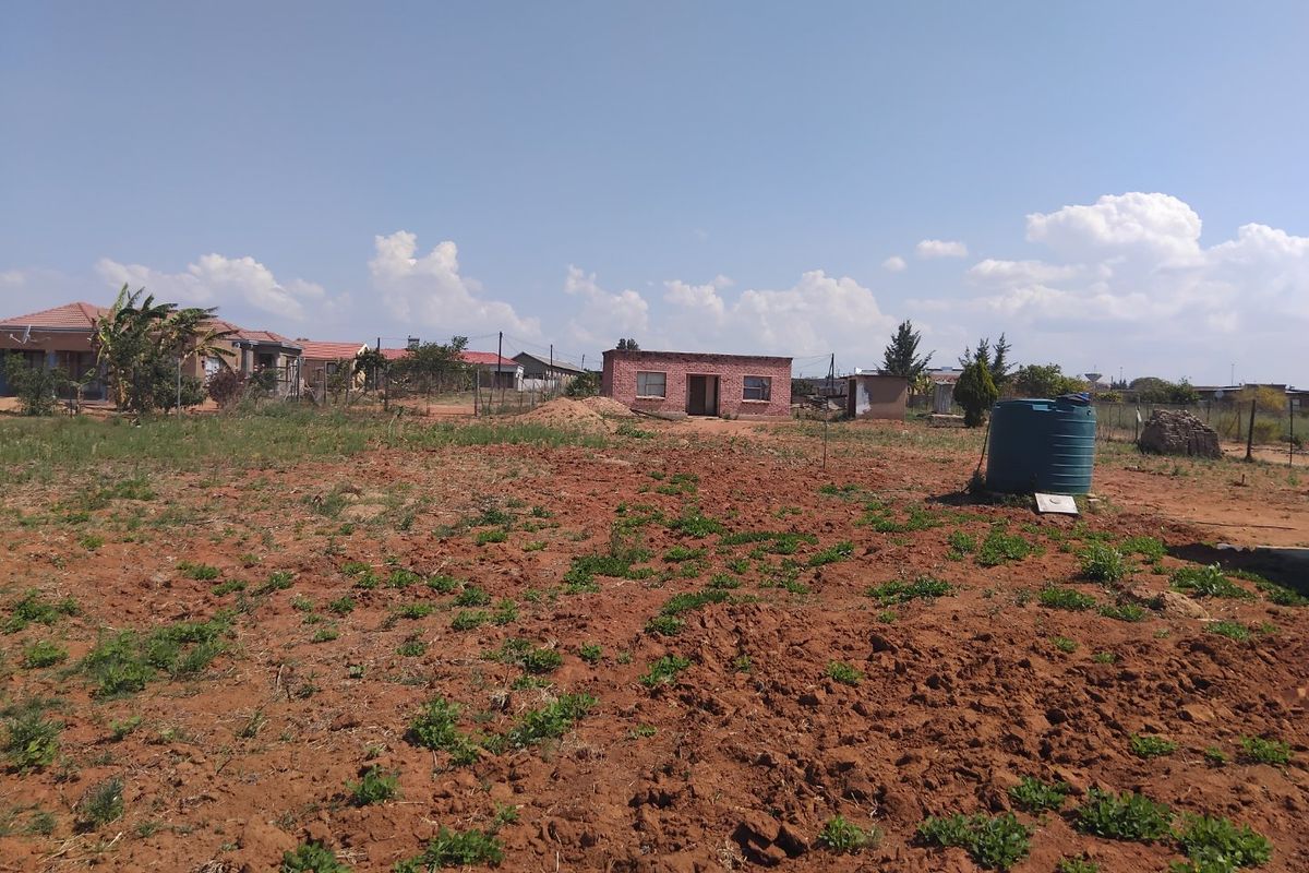 A view of a vacant residential plot featuring a water storage tank and an existing small structure in the background.
