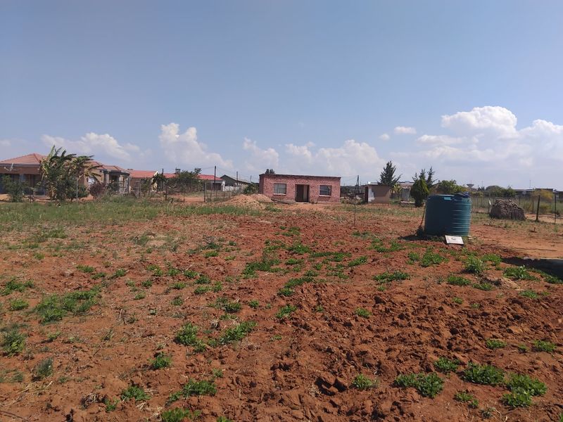 A view of a vacant residential plot featuring a water storage tank and an existing small structure in the background.