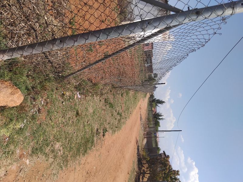A view of an unpaved access road bordered by chain-link fencing, showing the current state of the vacant land residential property.