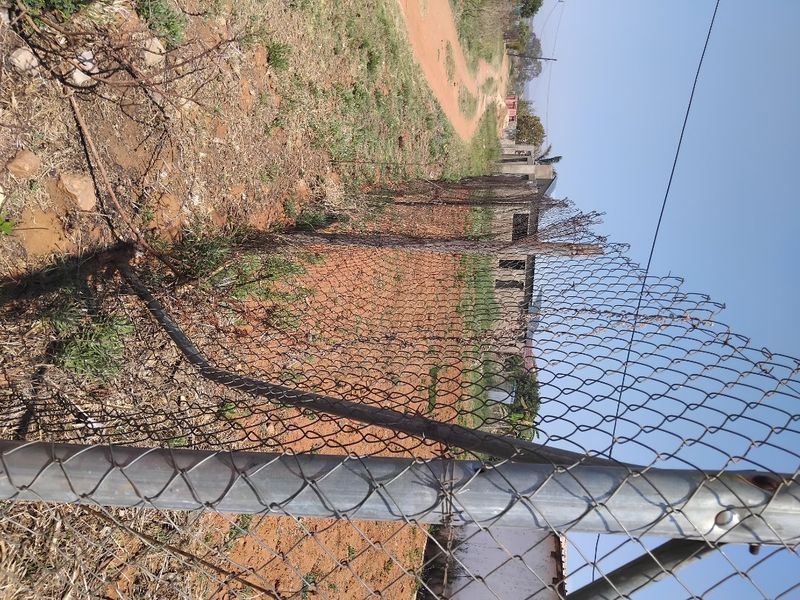 A view of a vacant residential plot featuring chain-link perimeter fencing and an unpaved access road.
