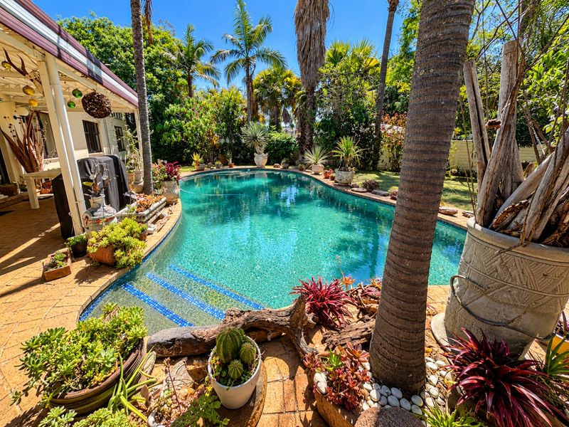 A well-maintained swimming pool area featuring a tiled patio, lush garden surroundings, and mature palm trees, creating a private outdoor oasis.