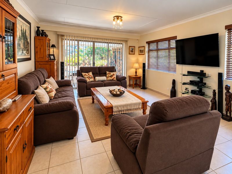 A comfortable living room featuring tiled flooring, large sliding glass doors leading to the patio, and venetian blinds.