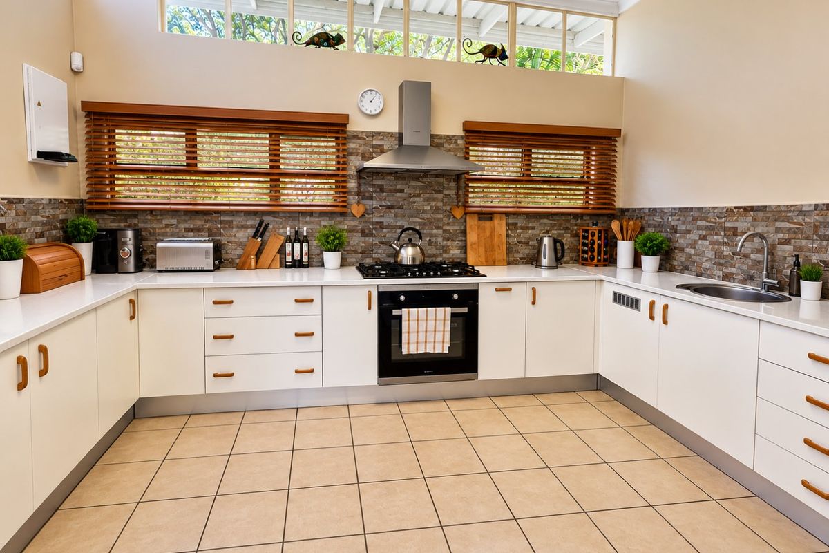 A well-maintained kitchen featuring white cabinetry, stone countertops, a gas hob with extractor fan, and a tiled splashback with natural light from clerestory windows.