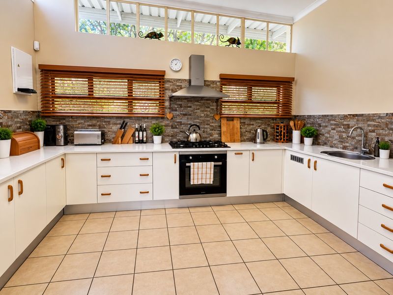 A well-maintained kitchen featuring white cabinetry, stone countertops, a gas hob with extractor fan, and a tiled splashback with natural light from clerestory windows.