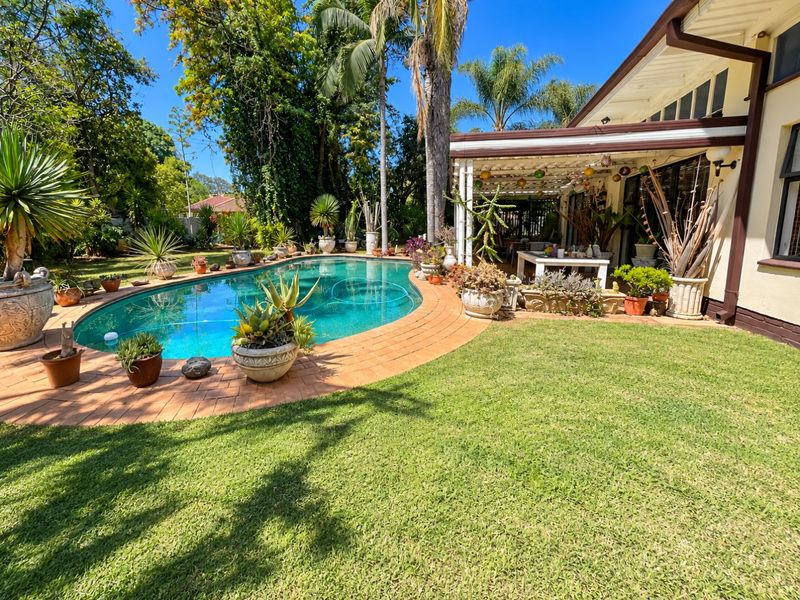 A well-maintained backyard featuring a swimming pool with brick coping, a lush lawn, and a covered patio area perfect for outdoor relaxation.