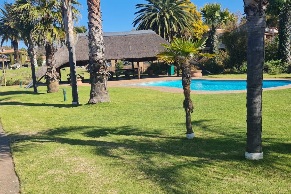 A well-maintained communal pool area featuring a thatched lapa, paved walkways, and established palm trees set within a landscaped garden.