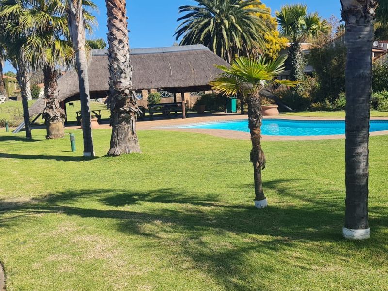 A well-maintained communal pool area featuring a thatched lapa, paved walkways, and established palm trees set within a landscaped garden.