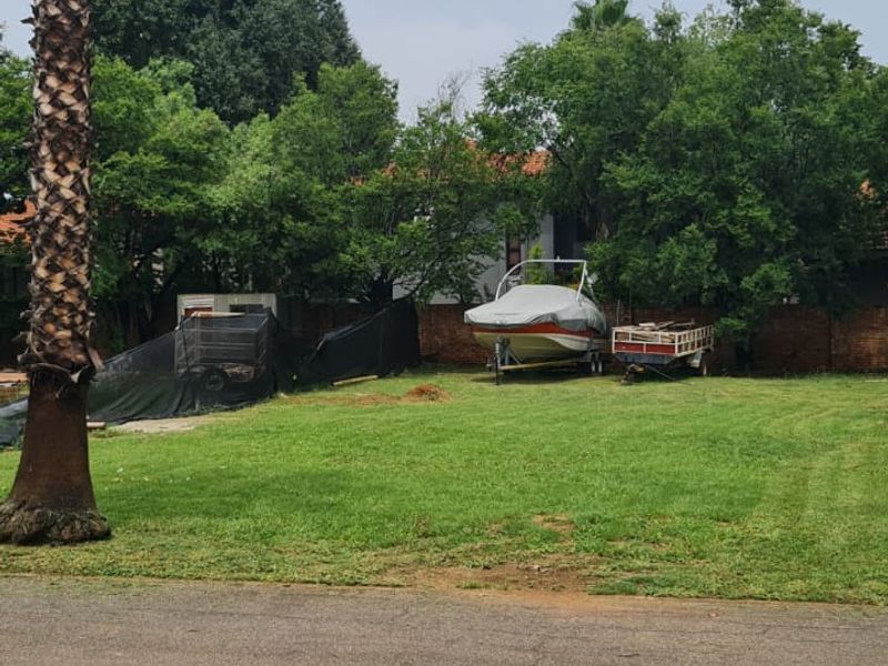A vacant residential plot featuring a level grassed area, mature palm tree, and established boundary walling, offering a clear space for future development.