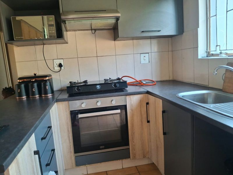 A functional kitchen featuring built-in cabinetry, a gas hob with oven, extractor fan, and a stainless steel sink with tiled backsplash.