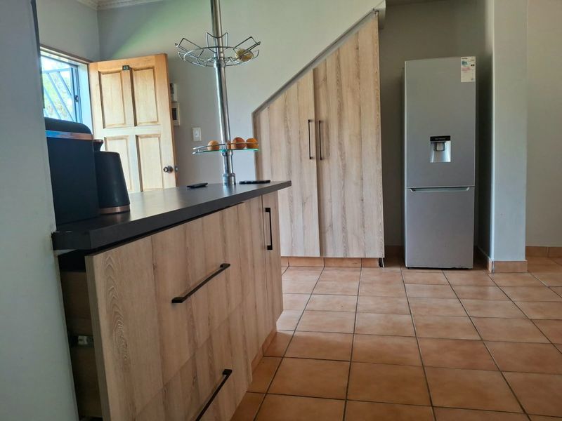A functional kitchen area featuring light wood-finish cabinetry, dark countertops, and tiled flooring, with convenient under-stair storage integration.