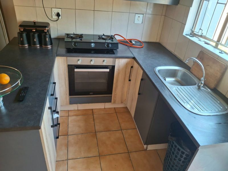 Compact kitchen featuring built-in oven, gas hob, stainless steel sink, and modern laminate cabinetry with tiled backsplash and flooring.