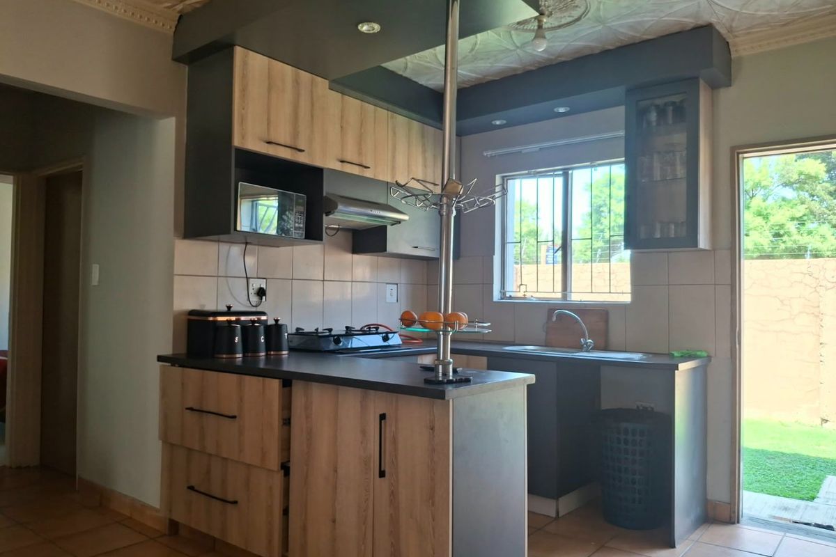 A functional kitchen featuring modern wood-look cabinetry, dark countertops, a gas hob with extractor, and direct access to the rear garden area.