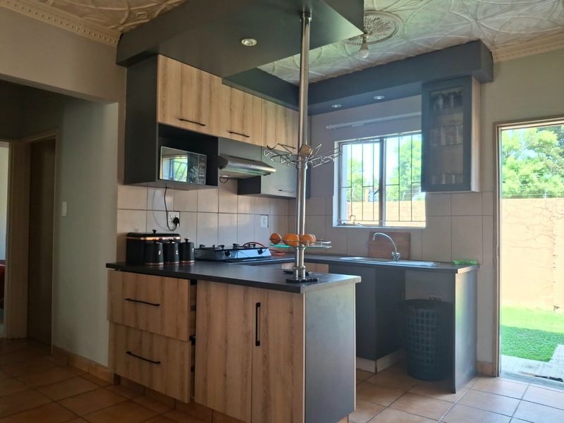 A functional kitchen featuring modern wood-look cabinetry, dark countertops, a gas hob with extractor, and direct access to the rear garden area.