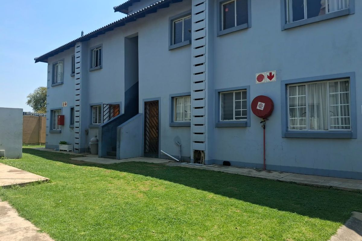 Rear view of a multi-story apartment building featuring a lawn, paved walkways, and essential fire safety equipment installed on the exterior wall.