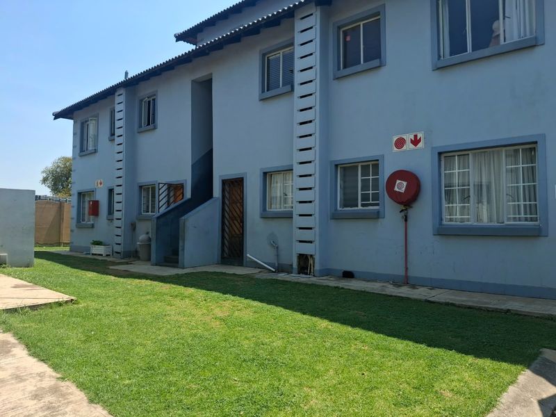 Rear view of a multi-story apartment building featuring a lawn, paved walkways, and essential fire safety equipment installed on the exterior wall.