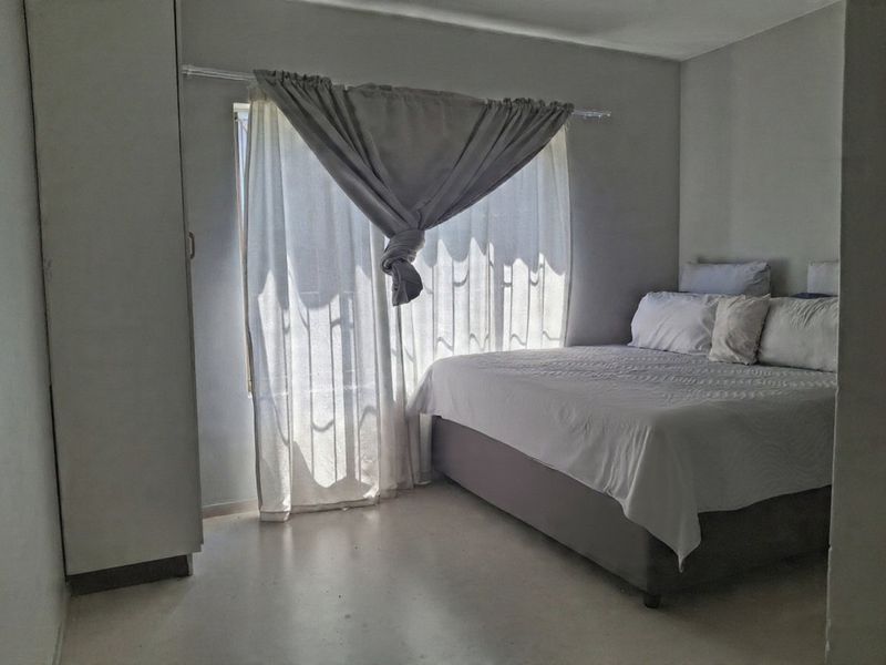 A simple bedroom featuring a built-in wardrobe and natural light from a window with curtains.